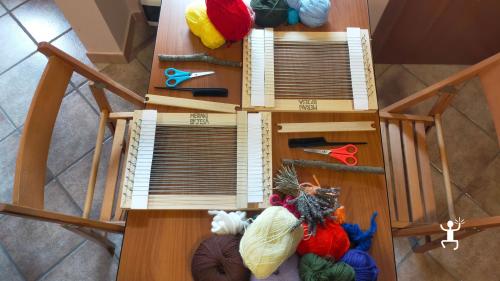 Tavolo visto dall’alto con due telai a cornice, gomitoli di vari colori e strumenti per la tessitura nella bottega di Bisaccia.