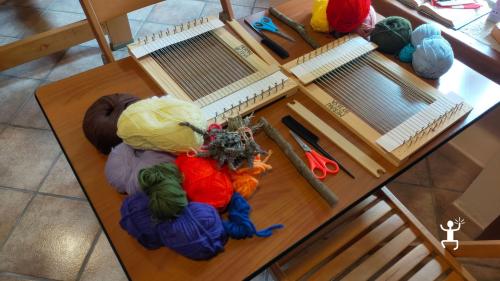 Due telai a cornice in legno con gomitoli colorati, forbici e pettini sul tavolo del laboratorio di tessitura a Bisaccia.