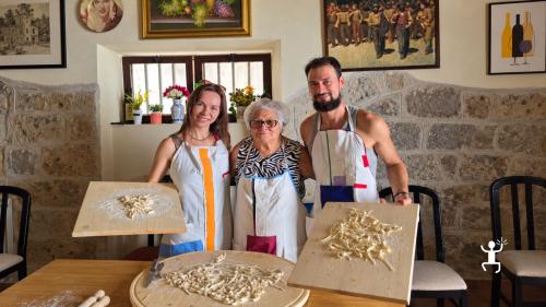 Una cuoca locale affianca una partecipante con abito tradizionale colorato nella lavorazione dell’impasto su una spianatoia a Castel Morrone
