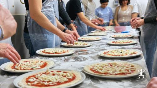 Pizze con pomodoro e mozzarella allineate sul banco mentre i partecipanti completano il condimento