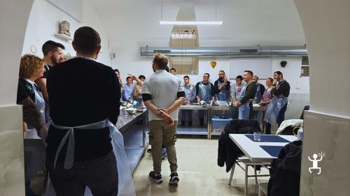 Partecipanti riuniti intorno al banco aggiungono gli ingredienti alle proprie pizze durante il corso a Napoli.