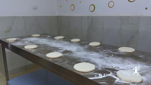Basi di pizza stese e allineate su un banco di acciaio cosparso di farina