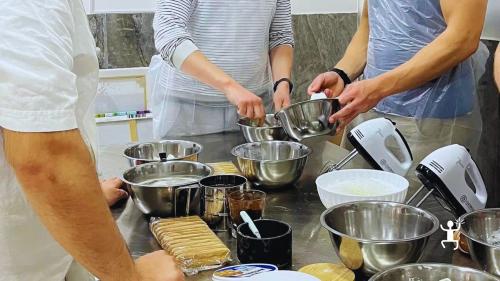 Partecipanti con grembiule lavorano gli ingredienti in ciotole di acciaio durante il corso di tiramisù a Napoli.