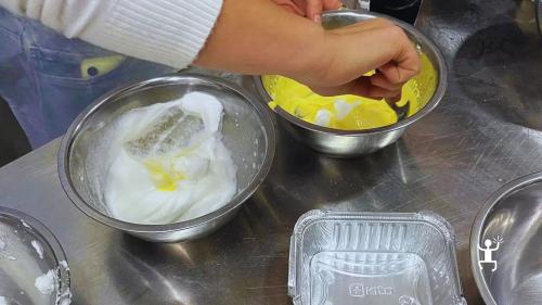 Una partecipante separa tuorli e albumi in due ciotole di acciaio durante la preparazione del tiramisù.