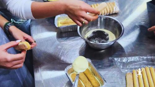 Una partecipante intinge un savoiardo nel caffè, accanto alla crema e agli altri biscotti sul banco.