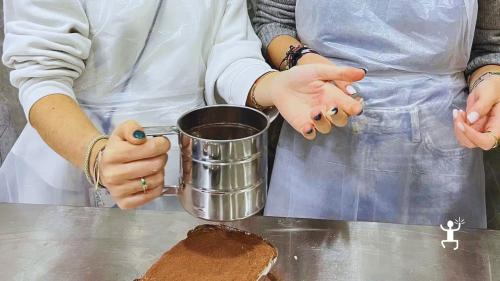 Una partecipante usa un setaccio per spolverare il cacao sul tiramisù appena preparato