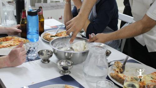 Partecipanti raccolgono il gelato da una ciotola di acciaio al centro di un tavolo con piatti di pizza.