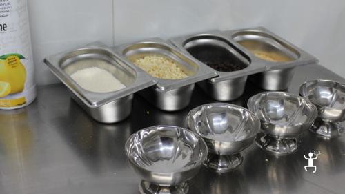 Coppette vuote in acciaio accanto a vaschette con granella e gocce di cioccolato sul banco del laboratorio di gelato a Napoli.