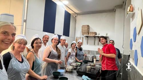 Gruppo di partecipanti con grembiuli e cappelli da cuoco intorno a un banco con ciotole e fruste elettriche durante una cooking class a Napoli.