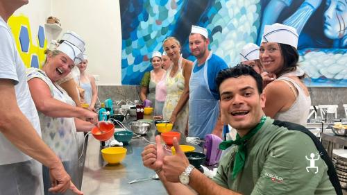 Gruppo di partecipanti con grembiuli e cappelli da cuoco posa accanto allo chef in giacca nella cucina del laboratorio a Napoli.