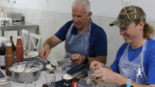 Due partecipanti con grembiule decorano le proprie coppette di gelato con gocce di cioccolato e granella durante il laboratorio a Napoli.