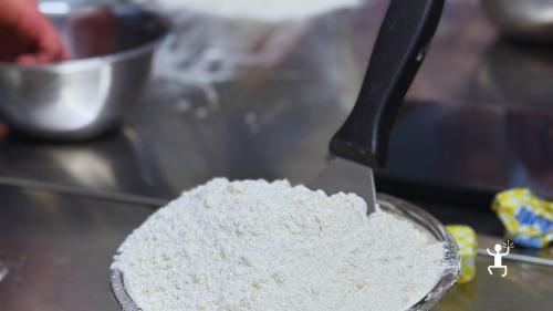 Primo piano di una paletta colma di farina durante la preparazione dell’impasto della pizza.
