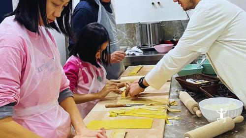 Ein Koch hilft einer Frau und einem Mädchen bei der Zubereitung von Ravioli während des Pastakurses in Neapel.